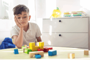 A little boy, sad and tired, plays with wooden blocks